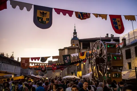 Gente disfrutando del mercado de las tres culturas Zaragoza, con pendones y una noria de madera.