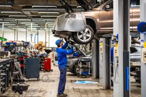 Mekaniker arbetar under en bil på en lyft i en auktoriserad verkstad. Verkstaden är full av verktyg och utrustning.