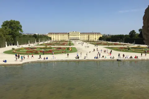 Piękny pałac Schönbrunn i jego ogrody, symbol wiedeńskiej historii. Ludzie spacerują pośród kwiatów i przy stawie.