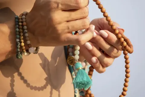 Manos sostienen un japa mala de 108 cuentas de madera. El japa mala 108 cuentas significado se asocia con la meditación y la conexión espiritual.