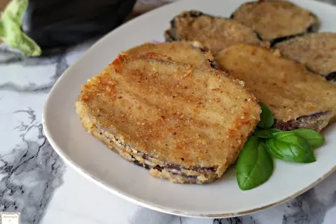 Fette dorate di cordon bleu di melanzane, impanate e fritte, servite su un piatto bianco con foglie di basilico fresco.