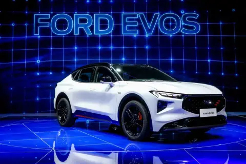 Biały Ford Evos na niebieskiej scenie z napisem "FORD EVOS" w tle.