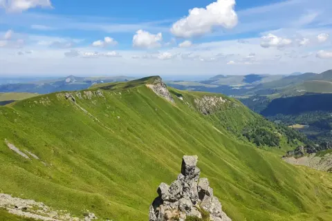 Zielone, faliste wzgórza Masywu Centralnego we Francji pod błękitnym niebem z chmurami.