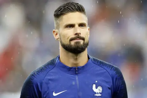 Olivier Giroud w deszczu, z charakterystycznymi fryzurami piłkarskimi i zarostem.