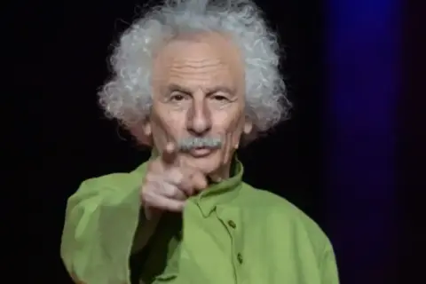El brujo del Teatro de las Esquinas, con su melena blanca y camisa verde, señala al público.