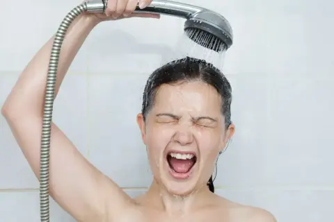 Une femme crie sous une douche froide, visiblement contrariée par un problème d'eau chaude.
