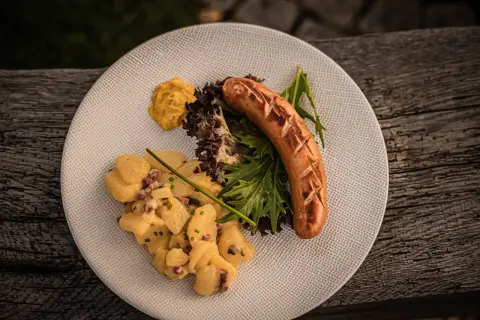 Herzhafter salat zur bratwurst mit Kartoffelsalat, Senf und frischem Grün auf einem Teller.