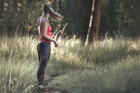 Frau im Laufoutfit im Wald. Sie genießt die Natur und die Ruhe, die das Joggen mit sich bringt.