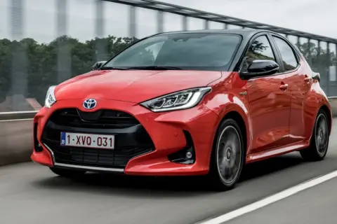Czerwony Toyota Yaris 1. generacji z czarnym dachem pędzi po drodze.