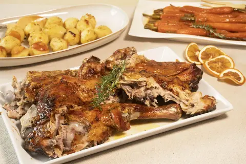Pierna de cordero lechal al horno jugosa, dorada y tierna, acompañada de patatas asadas y zanahorias glaseadas.