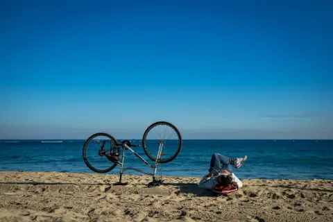 Odpoczynek po przejażdżce Velo Baltica. Rower na plaży, człowiek leży na piasku, patrząc na morze.
