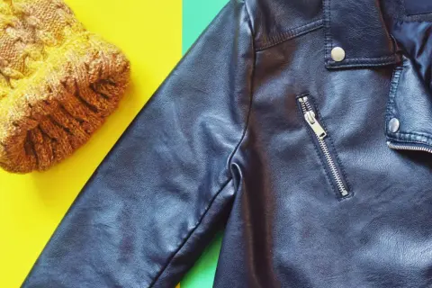 Veste en simili cuir noire et bonnet jaune sur fond coloré. Apprenez comment nettoyer une veste en simili cuir pour qu'elle reste comme neuve.