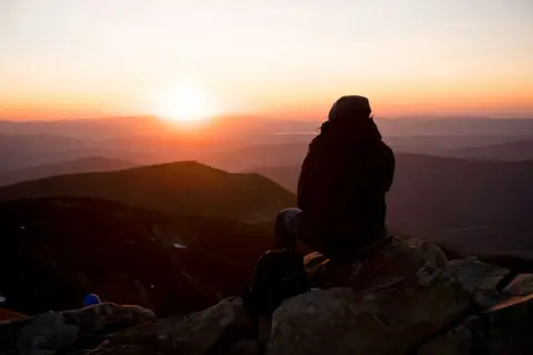 Sonnenuntergang in den Hohen Tatra. Eine Person sitzt auf einem Felsen und blickt auf die Berge.