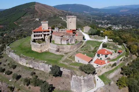 El imponente castillo de Monterrey se alza sobre una colina, rodeado de murallas de piedra y un paisaje verde.