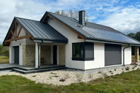Nowy, nowoczesny dom z panelami słonecznymi na dachu, kamienną okładziną i drewnianymi elementami. Gotowy do zamieszkania, posiada pozwolenie na użytkowanie.