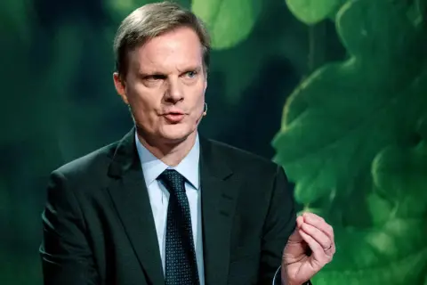 Jens Henriksson, VD för Swedbank, talar med en gest. Bakgrunden är grön med stora blad.