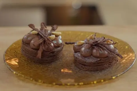 Dos bizcochos sin harina de chocolate, decorados con crema y avellanas, sobre un plato dorado.