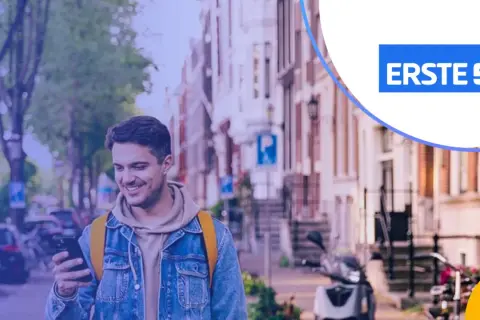 Uśmiechnięty mężczyzna z telefonem w ręku, w tle ulica z budynkami i skuterem. Promocja Santander lokata 3-miesięczna.