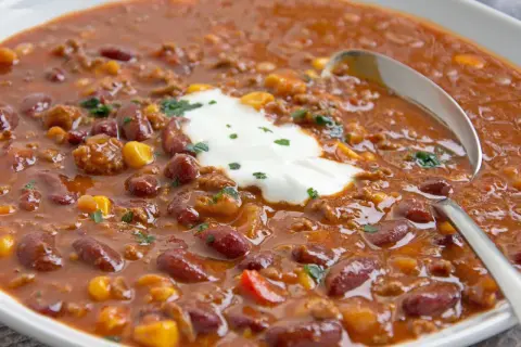 Herzhaftes Chili con Carne original mit Kidneybohnen, Mais und Hackfleisch, garniert mit einem Klecks saurer Sahne und Petersilie.