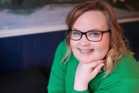 Kvinna med glasögon och grön tröja ler, trots morgonens ångest och depression.