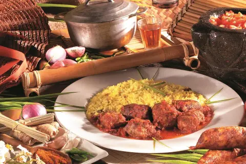 Un rougail saucisses traditionnel, servi avec du riz jaune, des tomates, des oignons et des épices.