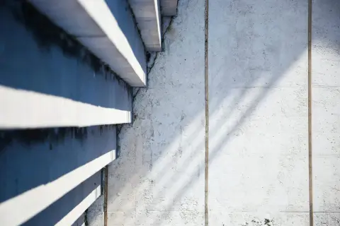 Ombre et lumière sur un mur en béton cellulaire, révélant des traces d'humidité et de légères fissures.