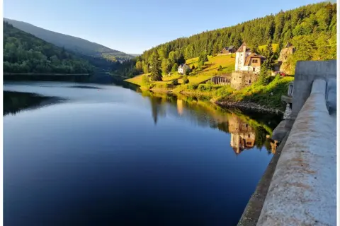 Spokojna tafla jeziora odbija zamek i zalesione wzgórza czeskich Karkonoszy.