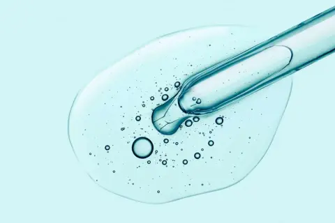 Tropfen Hyaluron-Serum aus Pipette auf hellblauem Hintergrund. Hilft gegen Pickel und spendet Feuchtigkeit.
