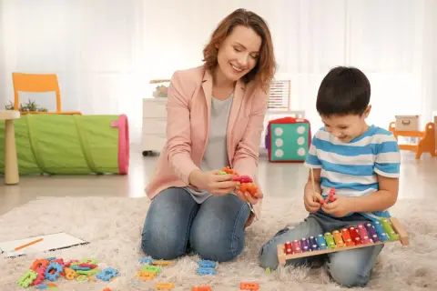 Psycholog dziecięcy i chłopiec bawią się klockami i cymbałkami na dywanie.