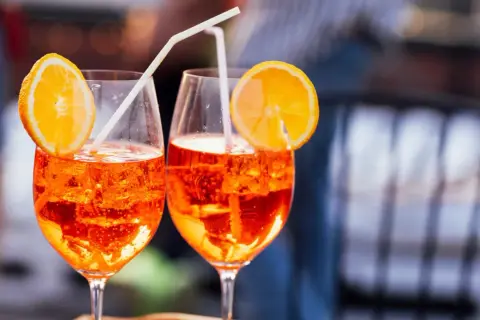 Dos Aperol Spritz refrescantes, con rodajas de naranja y pajitas, evocan el aperitivo italiano y su aperol spritz origen.