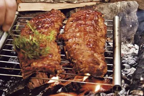 Två saftiga spareribs grillas över öppen eld. En hand lägger på en kvist rosmarin för extra smak.