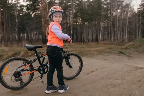 Dziewczynka w kasku i kamizelce pomarańczowej stoi obok roweru, gotowa na egzamin na kartę rowerową.