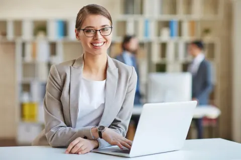 Lächelnde Frau mit Brille am Laptop, bereit für ihre medizinische Schreibkraft Ausbildung.