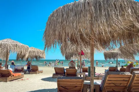 Słoneczne wakacje w Rumunii nad Morzem Czarnym. Leżaki i parasole z trawy na piaszczystej plaży, w tle kąpielowicze.