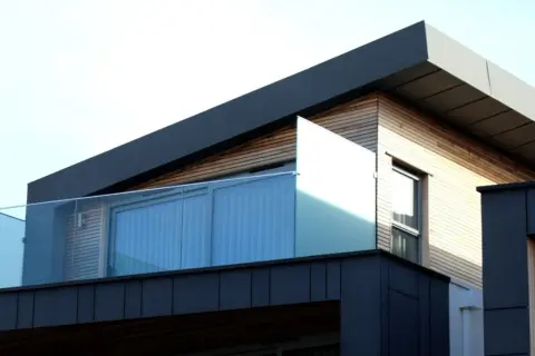 Nowoczesny budynek z drewnianą elewacją i szklanymi balustradami. Widać fragment dachu, który sugeruje, jak zrobić spadek na dachu płaskim.