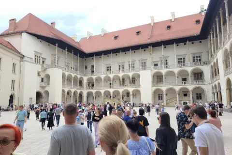 Tłum turystów zwiedza dziedziniec Wawelu, podziwiając renesansową architekturę. Warto zobaczyć na Wawelu to miejsce pełne historii.