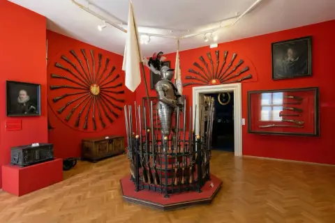 Armure de chevalier et fusils anciens exposés dans une salle rouge vif, un aperçu de l'interieur chateau de Prague.