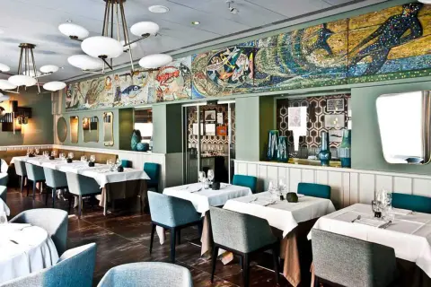 Interni eleganti di un ristorante, con tavoli apparecchiati e un grande mosaico marino sul muro. Un luogo ideale per scoprire i migliori ristoranti di pesce a Milano.