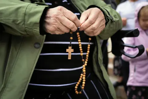 Dłoń starszej osoby trzyma paciorki różańca, odmawiając modlitwę do anioła stróża za dorosłe dzieci.