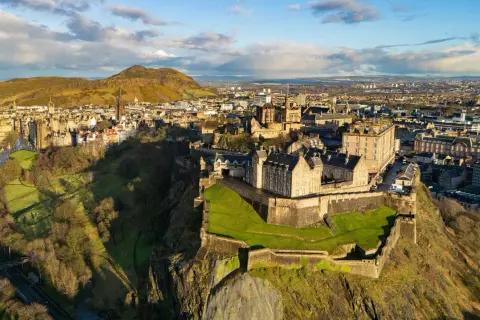 Edinburgh Castle tronar över staden, Skottlands huvudstad. En historisk vy med gröna kullar och moln på himlen.