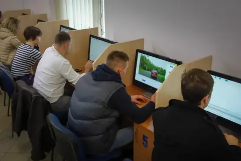 Ludzie siedzą przy komputerach, rozwiązując testy. Tak sprawdzisz, jak zdałeś egzamin teoretyczny na prawo jazdy.