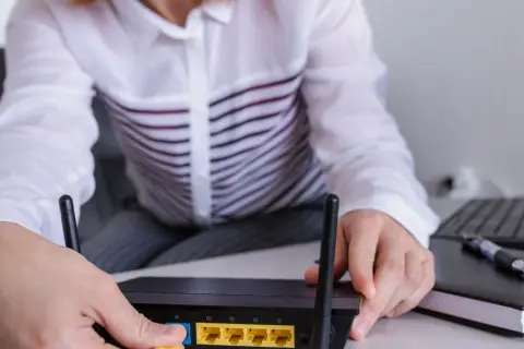Ręce podłączają kabel do routera, pokazując, jak wejść na router. Obok leży laptop i notatnik.