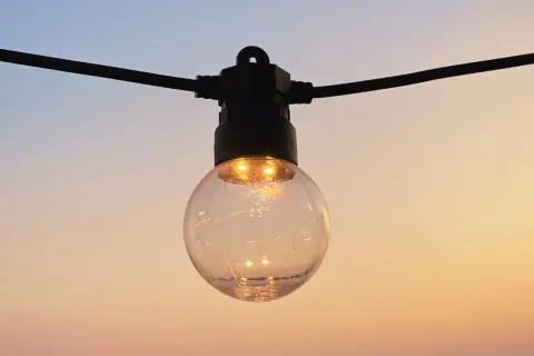 Guirlande lumineuse extérieure, une ampoule sphérique éclairée sur fond de ciel crépusculaire. La définition IP protection garantit sa résistance.