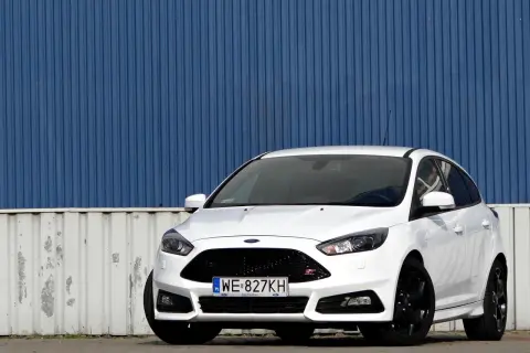 Biały Ford Focus ST z silnikiem 2.0 TDCI, zaparkowany przed niebieską, falistą ścianą.