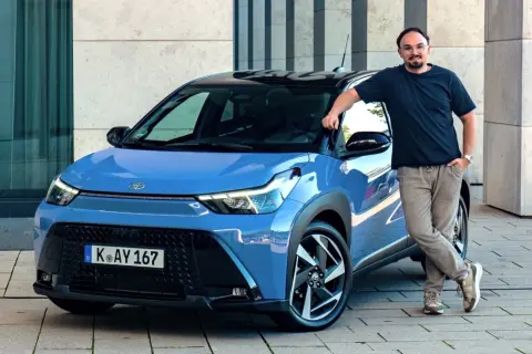 Mężczyzna opiera się o niebieską Toyotę Aygo X Hybrid.
