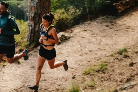 Deux coureurs s'entraînent sur un sentier de montagne, profitant d'un entraînement fractionné trail dans un paysage verdoyant.