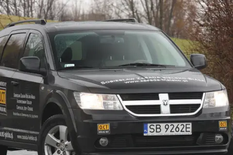 Czarny Dodge Journey z naklejkami "OCT UWOLNIJ MOC" i "Sobiesław Zasada Bielsko-Biała".