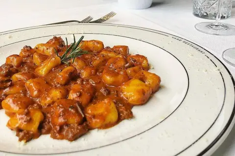 Gnocchi al ragù, un classico tra i piatti tipici maceratesi, serviti su un piatto bianco con rosmarino fresco.