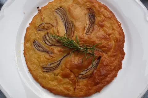 Herzhafte Kichererbsenmehl Rezepte: Goldbrauner Kuchen mit roten Zwiebeln und Rosmarin auf weißem Teller.