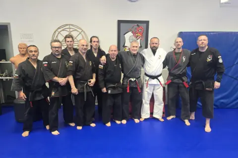 En grupp män i svarta och vita dräkter poserar på en blå matta. De är en del av en kenpo karate-klubb.